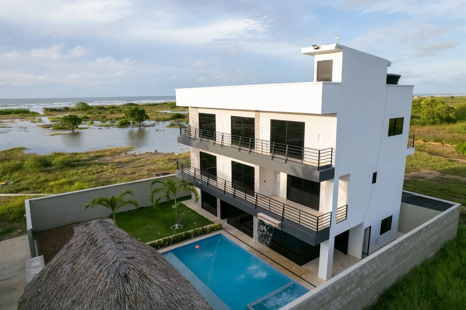 Vista aérea de Playa Candela: casa hotel de tres pisos con piscina, kiosco de palma y el mar Caribe al fondo